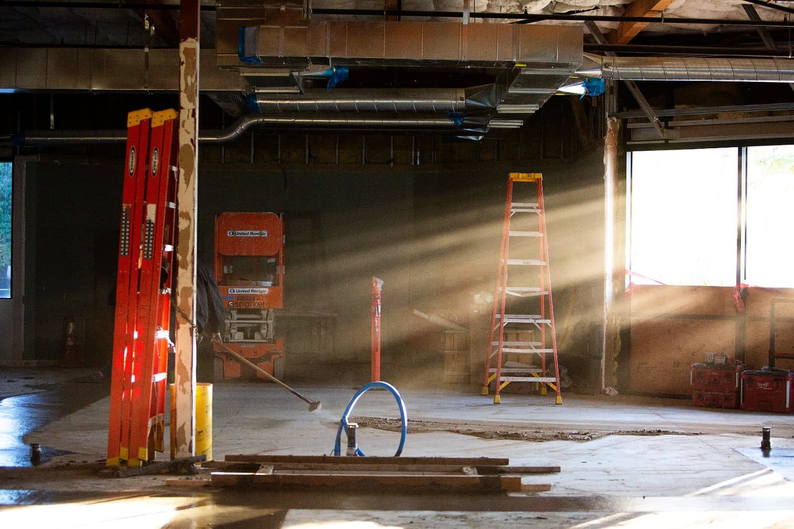 Sunlight streaming into a gutted interior with orange ladders and a scissor lift